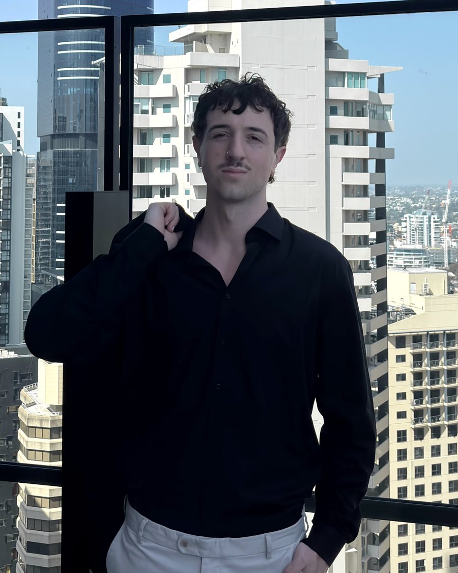 Kyle Hartwell, Founder and Director of Hartwell Digital, standing on a high balcony with the Brisbane city skyline behind him